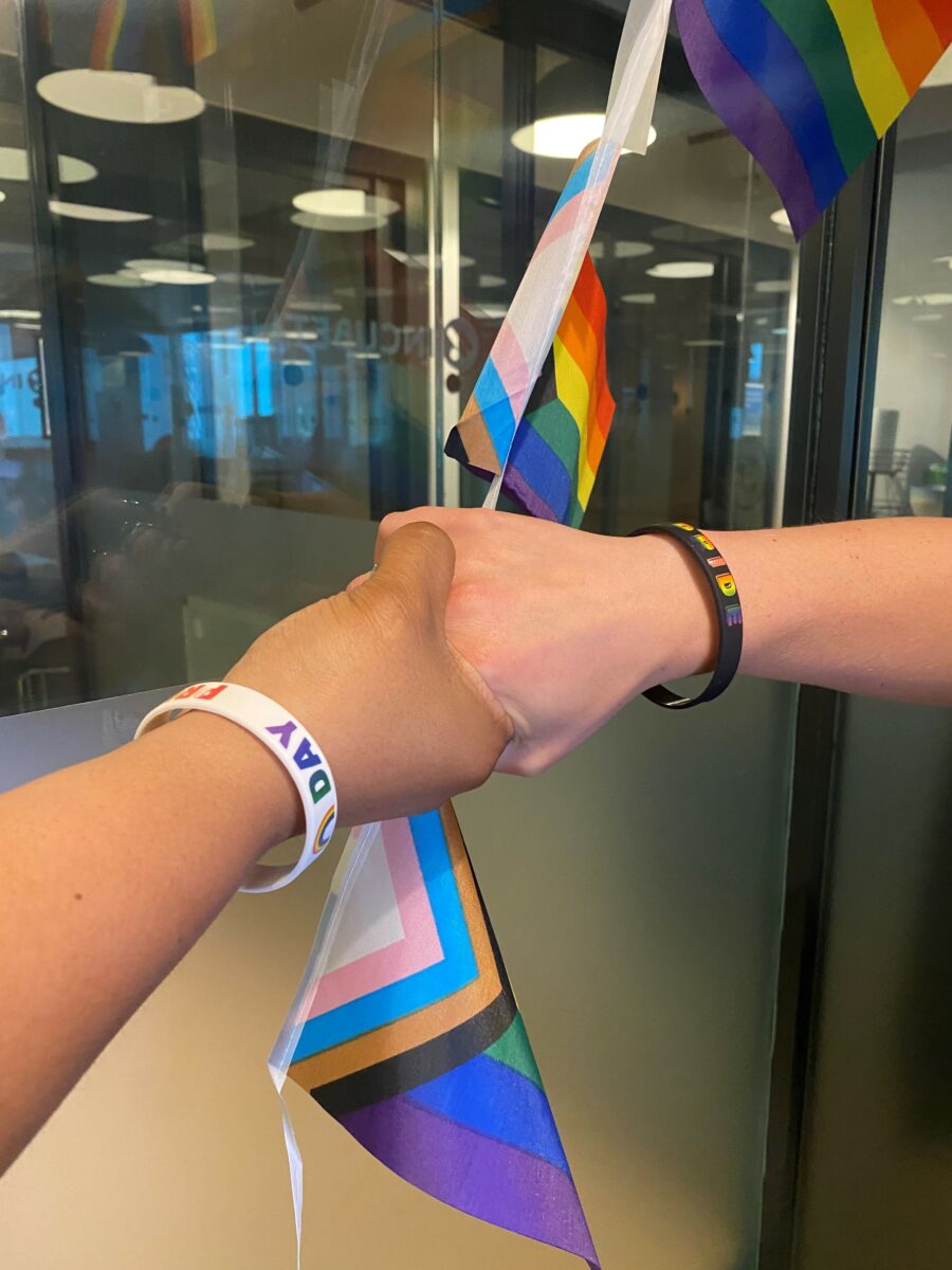 Two hands holding whilst wearing Pride wristbands