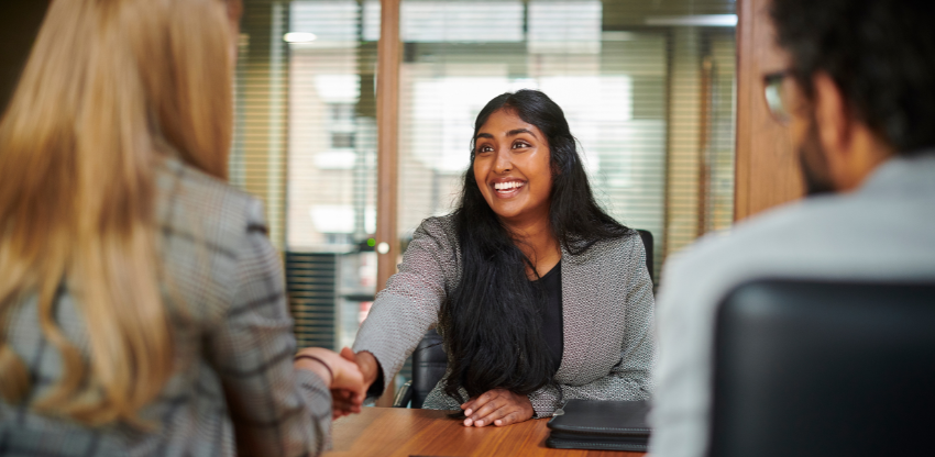 Person in focus shaking hands with one of two interviewers over a desk