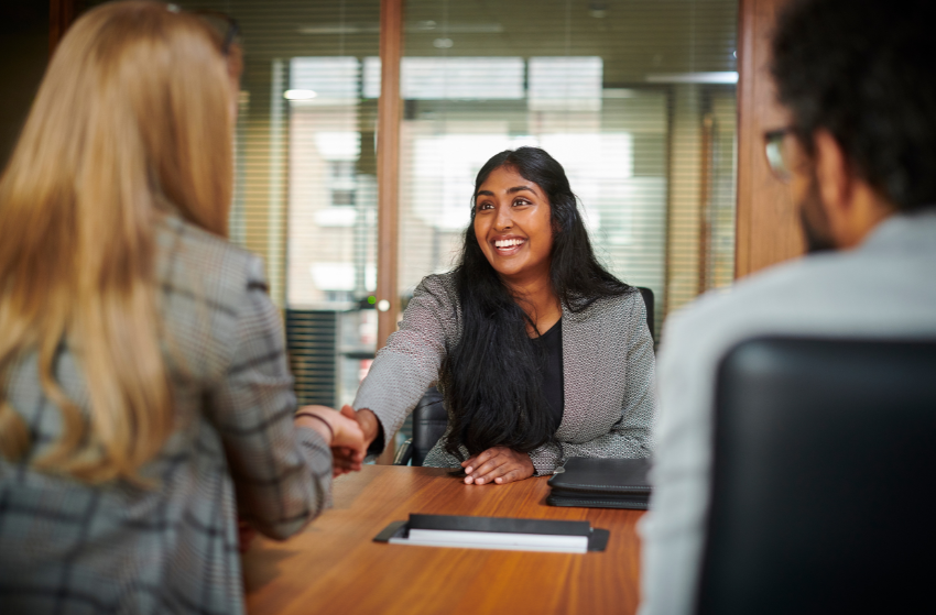 Person in focus shaking hands with one of two interviewers over a desk